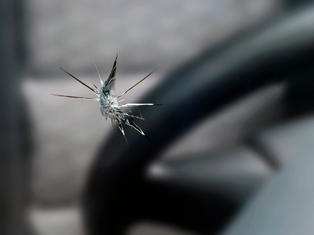 Close-up of a stone chip in a car windshield with fine cracks visible on the driver's side