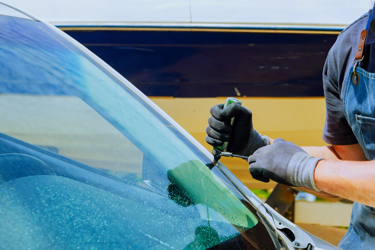 Technician replacing a damaged windshield using precision tools at an auto service centre