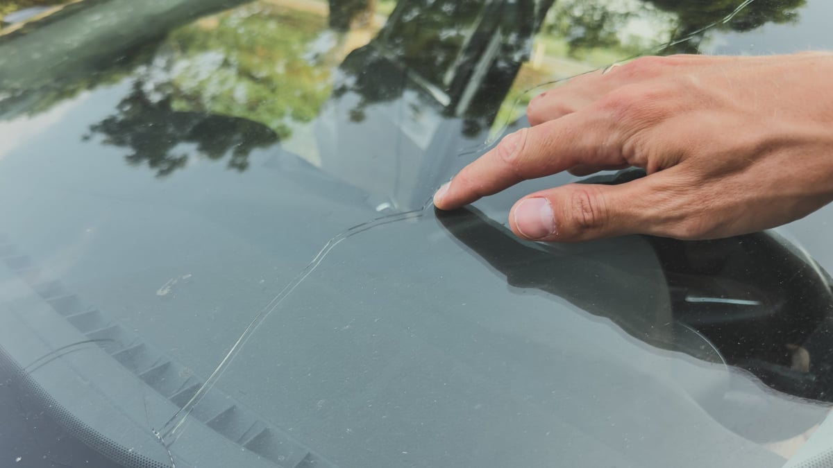 Hand pointing at a long crack running across a car windshield