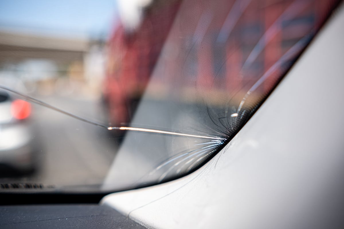 Close-up of a cracked windshield caused by a small rock strike on a highway