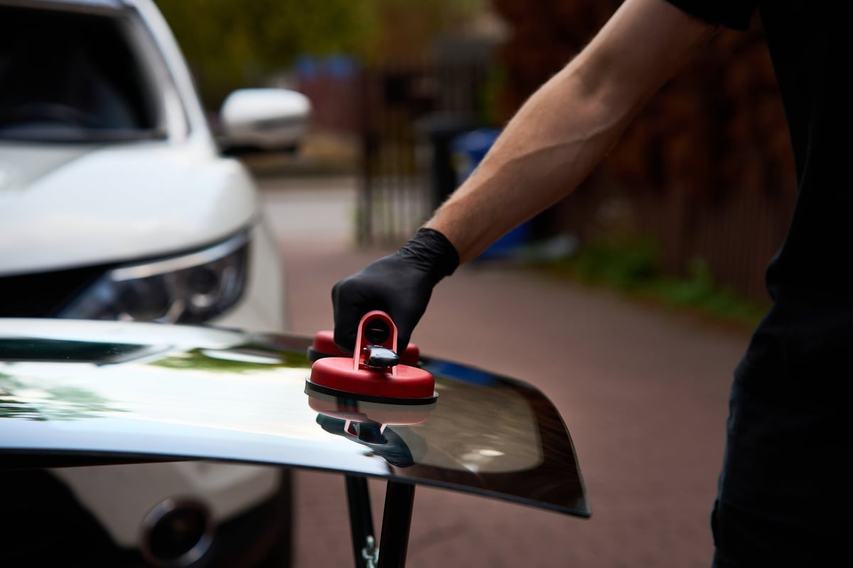 Red vacuum lifter holding new car glass on a stand before a mobile installation